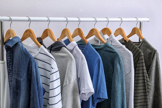 Stylish clothes hanging on wardrobe rack against light background