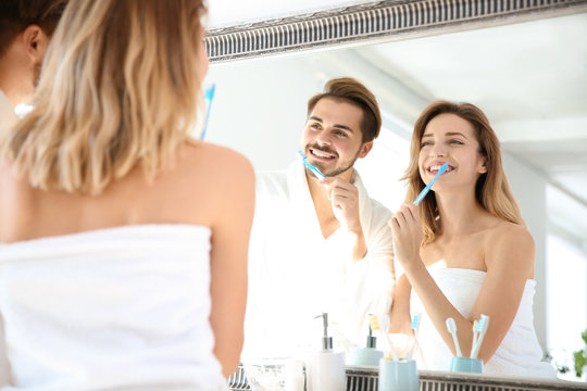 Young couple with toothbrushes near mirror in bathroom. Personal hygiene
