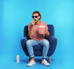 Fototapeta premium Emotional man with 3D glasses, popcorn and beverage sitting in armchair during cinema show on color background