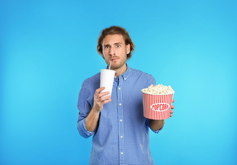 Emotional man with popcorn and beverage during cinema show on color background