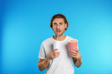 Fototapeta premium Emotional man with popcorn and beverage during cinema show on color background