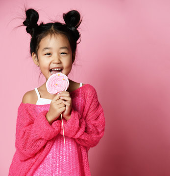 Happy young asian little girl kid lick eat happy big sweet lollypop candy on pink 