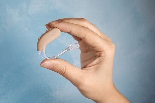 Woman holding hearing aid on color background, closeup