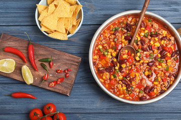 Delicious chili con carne served on wooden table, flat lay
