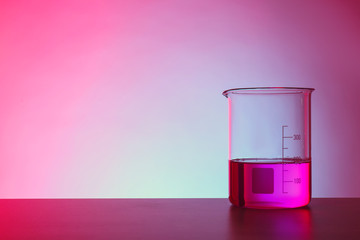 Beaker with liquid on table against color background. Chemistry laboratory glassware