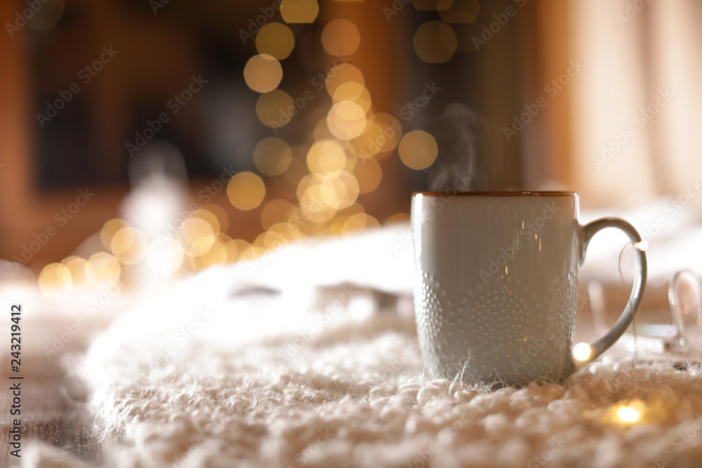 Sticker Cup of hot beverage on fuzzy rug against blurred background, space for text. Winter evening