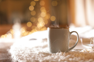 Obraz na płótnie Canvas Cup of hot beverage on fuzzy rug against blurred background, space for text. Winter evening