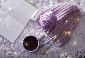 Flat lay composition with cup of hot beverage, knitting yarn and book on fuzzy rug. Winter evening