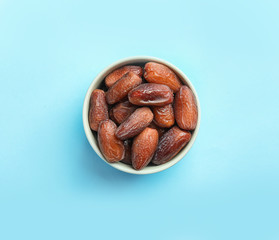 Bowl with sweet dried date fruits on color background, top view