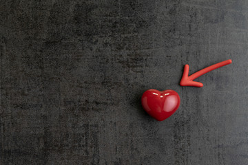 Red magnet arrow pointing to shiny ceramic red heart shape on cement chalkboard wall, minimal...
