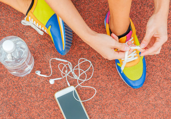 Sports woman runner tying shoelaces. Woman lacing her sneakers on a stadium running track.