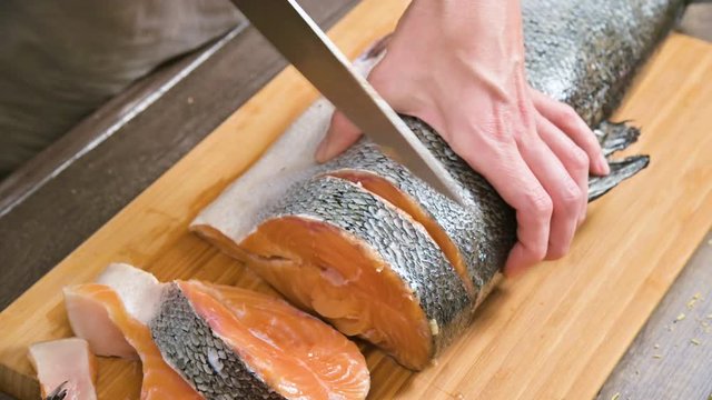 Close-up of female hands are cutting with a knife a large salmon on a wooden table of home cooking