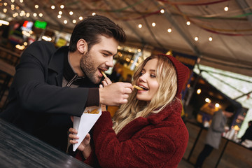 Close-up of young couple are eating french fries at the street food market.