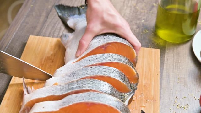 Close-up of female hands are cutting with a knife a large salmon on a wooden table of home cooking