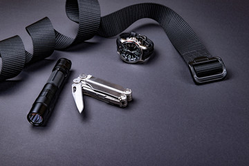 Everyday carry (EDC) items for men in black color - tactical belt, flashlight,  watch and silver multi tool.
