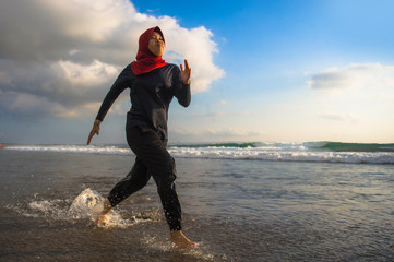young healthy and active runner Muslim woman in Islam hijab head scarf running and jogging on the beach wearing traditional arab sport clothes in fitness workout