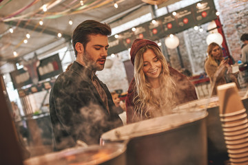 Close-up of young couple are drinking mulled wine at the street food market.