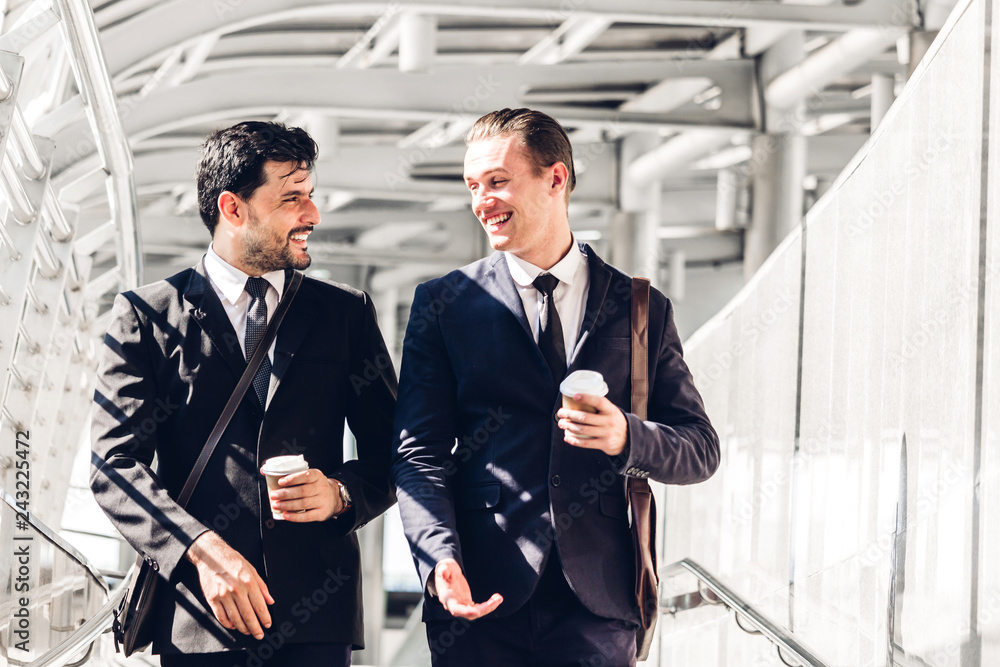 Wall mural two smiling businessman coworkers in black suit talking and walking.business people discussing strat