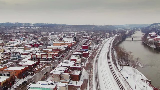A snowy winter forward aerial view of the business district of a typical Pennsylvania rust belt river town at Christmastime. Pittsburgh suburbs.  	