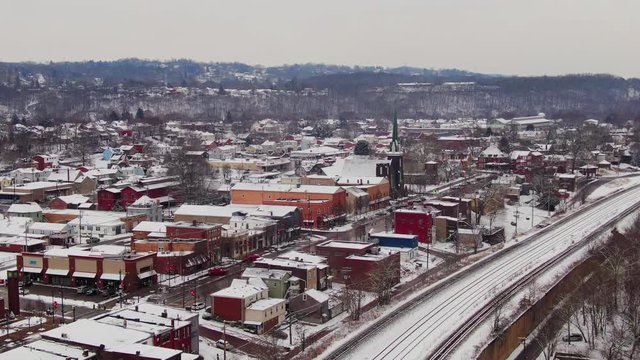 A snowy winter reverse aerial view of the business district of a typical Pennsylvania rust belt river town at Christmastime. Pittsburgh suburbs.  	