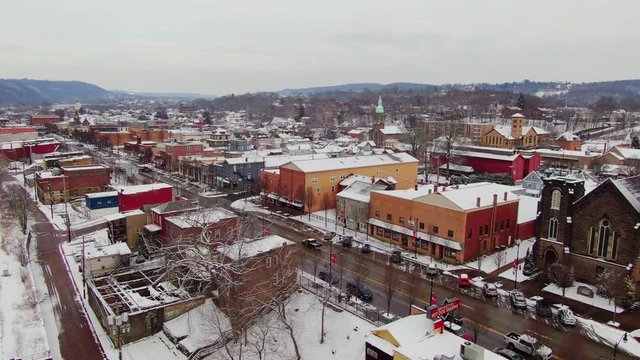 A snowy winter reverse aerial view of the business district of a typical Pennsylvania rust belt river town at Christmastime. Pittsburgh suburbs.  	