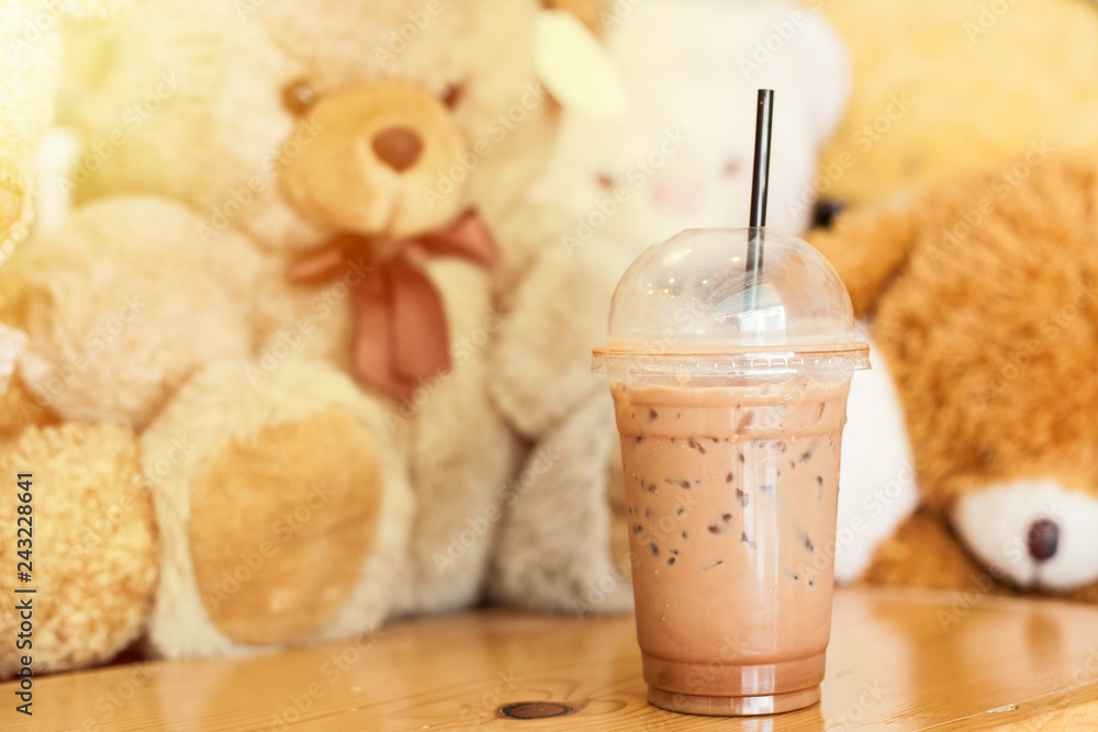 Wall mural cocoa cold with ice in the cup with straw put it on the wood table with bear doll in the cafe. - ima