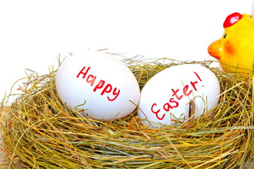 Two chicken eggs in straw nest with red text happy Easter next ceramic figurine of yellow hen on rough wooden board on white background. Close up