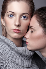 Two young women in gray sweaters on grey background. Beautiful girls stretching hands forward in embrace. Female friendship concept