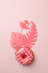 pink donut with icing and origami paper craft modern flowers decor, on pink background, monochrome close up