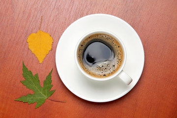 White cup with black coffee and autumn leaves