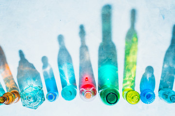 Glass bottle assortment with colorful shadows and flares on a white background with copy space. Geometric shapes in photography concept. Direct sunlight flat lay