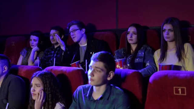 A group of young people watching a sad movie in the cinema, the girl is crying. Side view of a group of people in the cinema who watch a touching moment in an interesting movie.