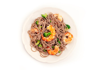 A plate of soba, buckwheat noodles, with shrimps and vegetables, shot from the top on a white background with copy space