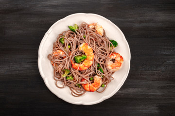A plate of soba, buckwheat noodles, with shrimps and vegetables, shot from the top on a black background with a place for text