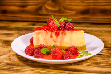 White plate with cheesecake New York, leaves of mint and raspberries on wooden table