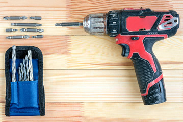 Electric screwdriver with bits and drills on wooden background. Construction tools concept. 