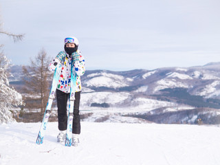 girl holding skis in her hands Happy girl holding skis and ski poles in hands, sitting in snow