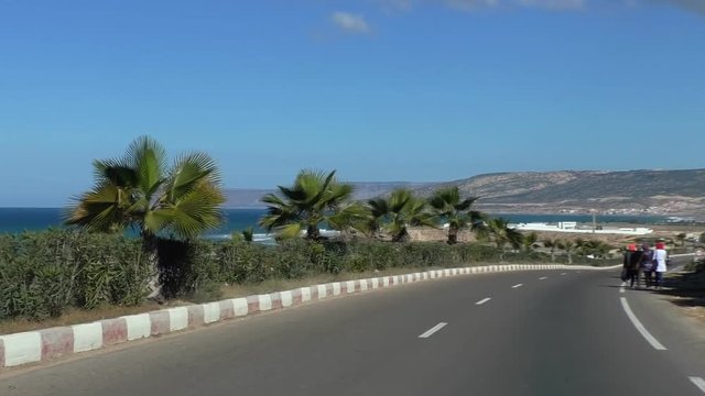 Car windshield view driving on Atlantic ocean seaside N1 highway. Passing by slow motorbike and young women pedestrians on the road