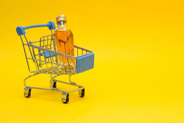 Small bottle with alcohol in a shopping basket, close-up, copy space, orange background, consumerism