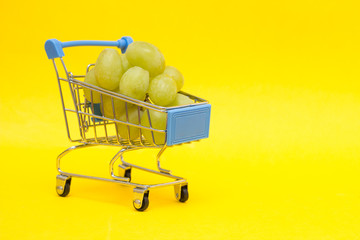 Grapes in a shopping trolley on a yellow background, close-up, copy space, sale