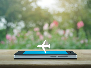 Airplane flat icon on modern smart mobile phone screen on wooden table over blur pink flower and tree in park, Business transportation online concept