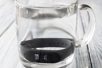 Black fitness watch (activity tracker), fitness bracelet, tracker with time and steps on display in the glass of water. Closeup, selective focus