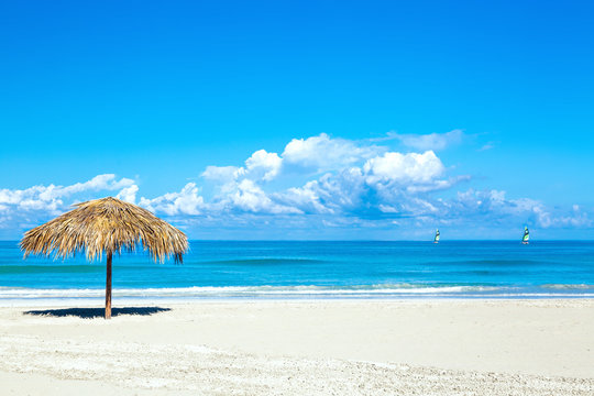 Straw umbrella on empty seaside beach in Varadero, Cuba. Amazing blue sky with clouds. Relaxation, vacation idyllic background.