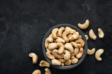 Cashew nuts in bowl on black background. Top view, copy space for text. Healthy snack, vegetarian food, beer snack