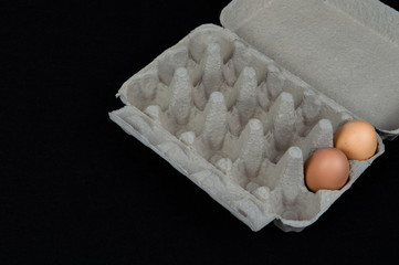 Fototapeta na wymiar Two chicken eggs in a carton box, isolated on black mat background