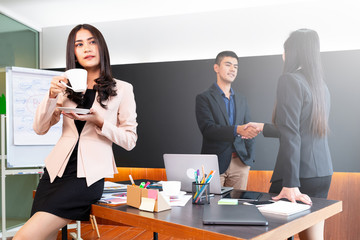 BUSINESS TEAM MEETING : Women hold coffee cup, business men and women check hand together in background