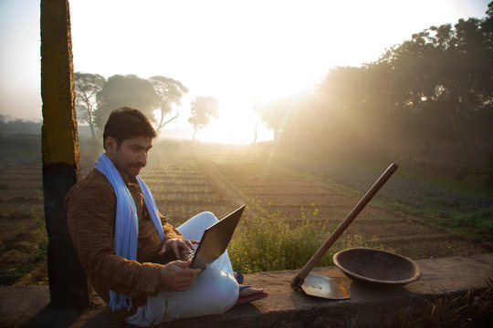 Farmer using laptop while sitting near his agriculture field