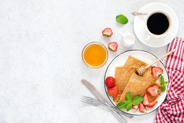 Crepes, thin pancakes or blini with strawberries, honey, coffee on concrete background. Top view, copy space for text