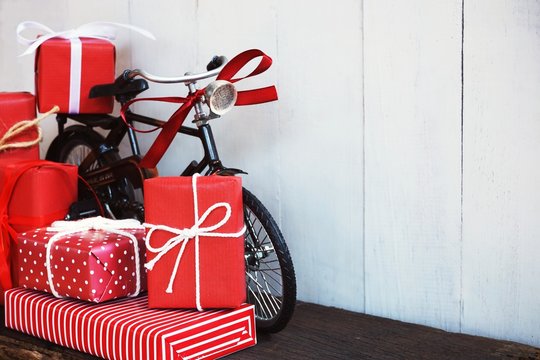 Group of elegant red gift box stack decorated with vintage toy bicycle on wood background, vibrant valentine lovely present concept
