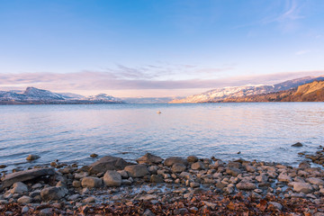 Rocky beach with lake and snow covered mountains at sunset